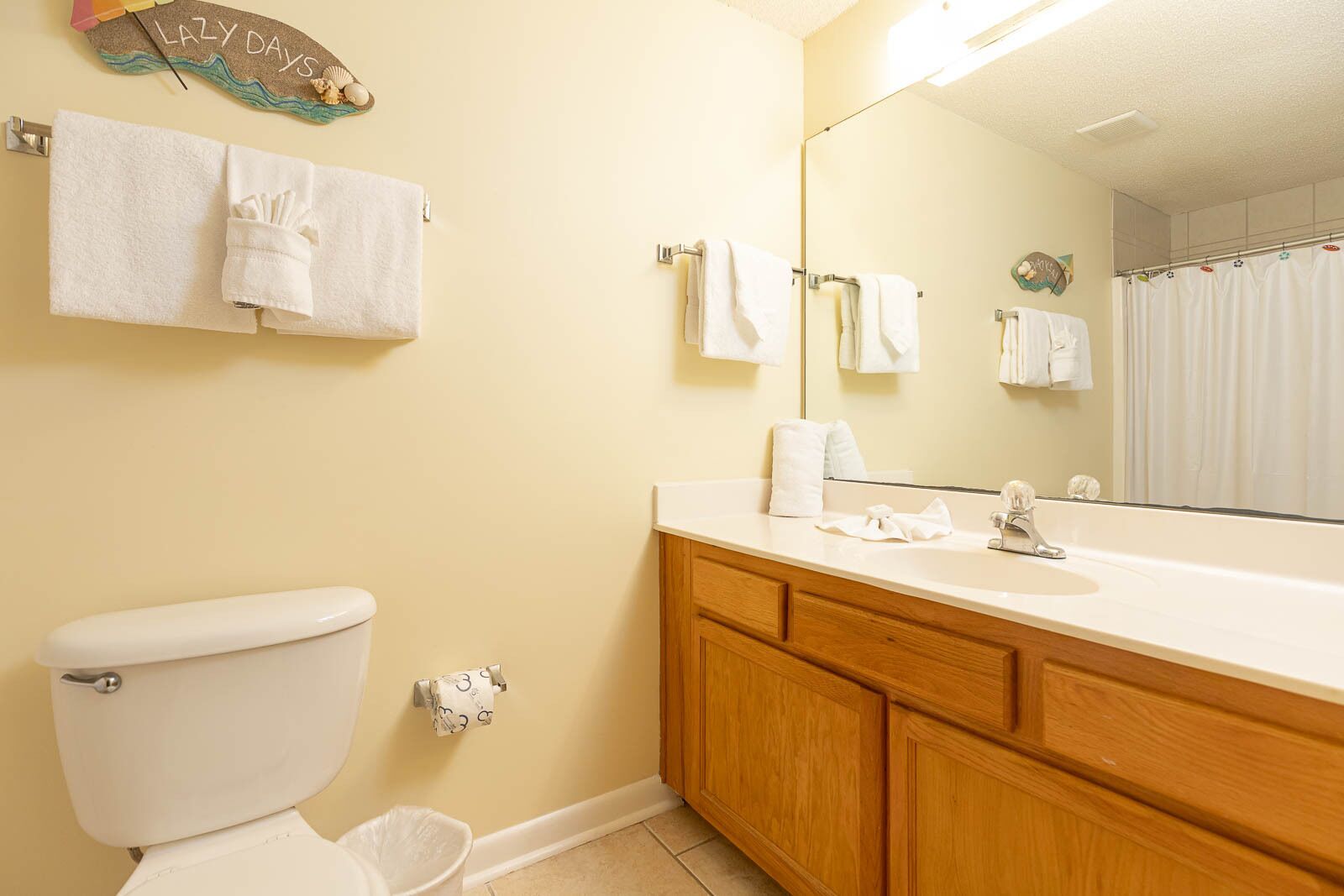 Un baño con inodoro, lavabo y espejo. Hay toallas colgadas en la pared y una cortina de ducha.