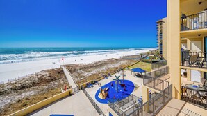 A beach view from a hotel balcony with a pool area and outdoor seating.