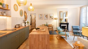 A modern kitchen with wooden countertops, a central island, and pendant lighting. There is a dining area with a table and chairs, and a fireplace.