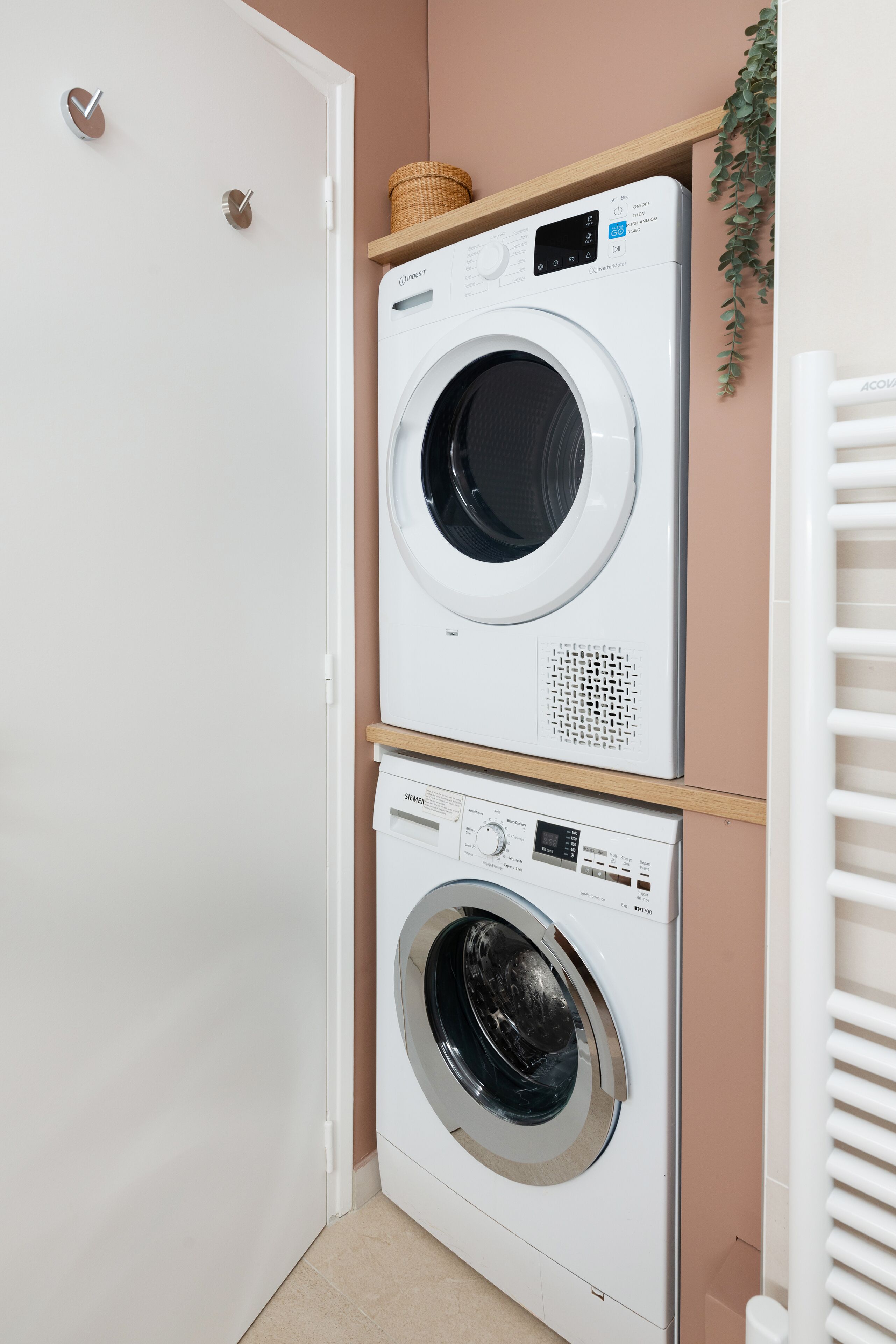 A laundry room with two stacked washing machines, a white door, and a plant on the wall.