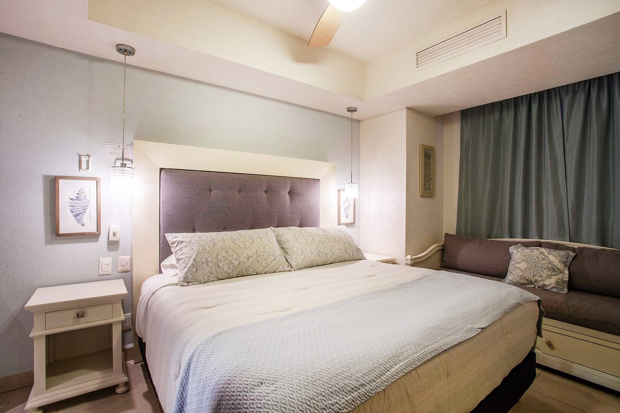 Una habitación de hotel con una cama grande, mesitas de noche, un sofá y una cortina.