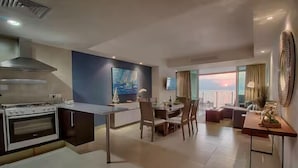 Una cocina moderna con una isla central, zona de comedor con sillas, un sofá y un televisor montado en la pared.