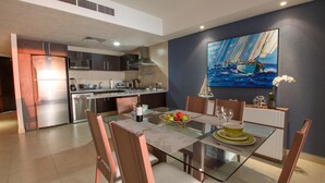 Una cocina moderna con electrodomésticos de acero inoxidable, un comedor con mesa de vidrio y un cuadro de un velero en la pared.
