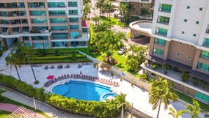 Un hotel moderno de gran altura con una piscina central rodeada de palmeras y un jardín paisajístico.