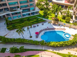 Et hotel med swimmingpool, udendørs siddepladser og frodig beplantning.