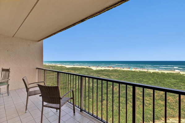 A balcony with wicker chairs overlooking a beach with a clear view of the ocean.
