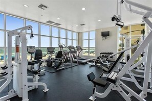 A gym with various exercise machines, large windows, and a clear view of the outdoors.