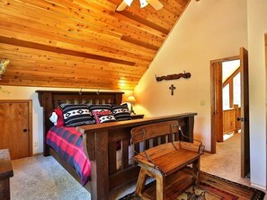 Ein Schlafzimmer mit Holzboden, einem Bett mit gemusterten Betttextilien, einer Bank und einem Kreuz an der Wand.