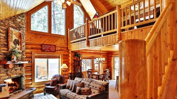 Ein Holzblockhaus-Interieur mit Kamin, einer Couch, einem Essbereich und einem Balkon.