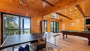 Uma cabana de madeira com mesa de pingue-pongue, mesa de bilhar e lareira de pedra.