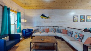 Een gezellige woonkamer met een houten plafond, een grote visdecoratie en een bank met kleurrijke kussens.