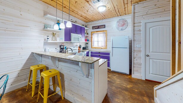Een keuken met houten wanden, een centraal eiland, paarse kastjes en een koelkast.