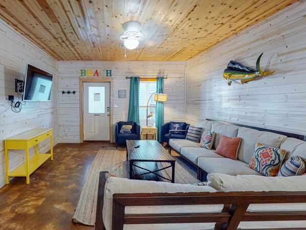 A cozy cabin interior with a wooden ceiling, a sofa, a coffee table, and a television on the wall.
