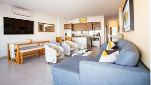 A modern living room with a grey sofa, a wooden dining table with benches, and a kitchen in the background. - Top Floor Condo with City View, Rooftop Pool, Gym in Old Town (Puerto Vallarta)
