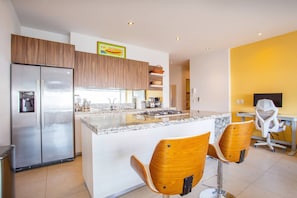 A modern kitchen with a built-in island, stainless steel appliances, and wooden bar stools. - Top Floor Condo with City View, Rooftop Pool, Gym in Old Town (Puerto Vallarta)