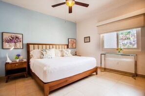 A bedroom with a wooden bed, a nightstand, a glass table, and a ceiling fan.