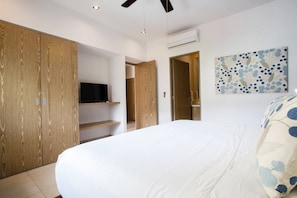 A bedroom with a bed, a television on a shelf, a wardrobe, and an air conditioning unit. - Top Floor Condo with City View, Rooftop Pool, Gym in Old Town (Puerto Vallarta)