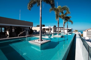 A pool area with clear blue water, palm trees, and modern buildings. - Top Floor Condo with City View, Rooftop Pool, Gym in Old Town (Puerto Vallarta)