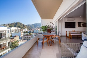 A balcony with a dining table, chairs, and a hanging chair.