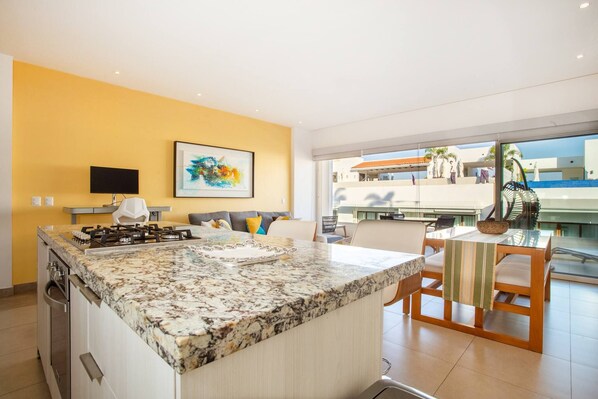 A modern kitchen with a granite countertop, a dining area with a table and chairs, and a large window offering a view of the outside. - Top Floor Condo with City View, Rooftop Pool, Gym in Old Town (Puerto Vallarta)