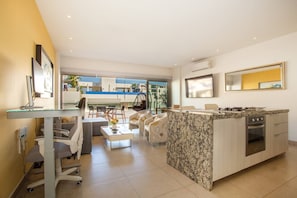 A modern kitchen with a marble island, a dining area with chairs, and a large window overlooking a pool. - Top Floor Condo with City View, Rooftop Pool, Gym in Old Town (Puerto Vallarta)