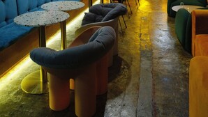 A cozy lounge area with a blue sofa, round tables, and a stage in the background. - Just Inn - City Hall (Taipei)