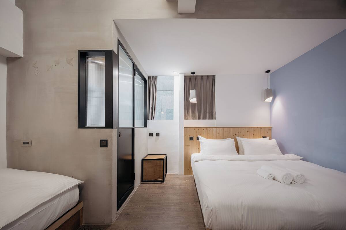 A modern hotel room with a wooden floor, a bed with white linens, a wooden headboard, and a small bedside table.