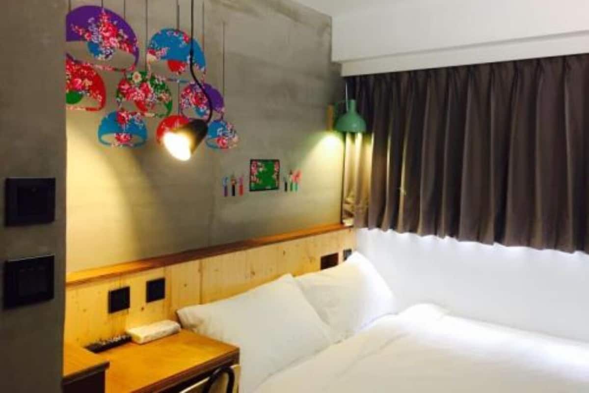 A hotel room with a bed, a wooden headboard, a nightstand, a lamp, and a wall with decorative hanging lights.