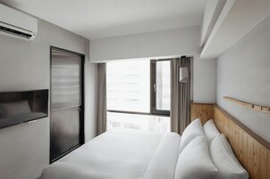 Een moderne hotelkamer met een groot bed, een ingebouwde televisie, een raam met gordijnen en een houten hoofdeinde.