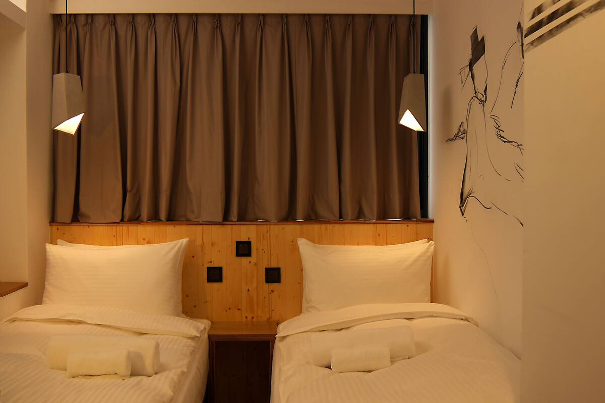 A hotel room with two beds, wooden headboard, and a large window with curtains.