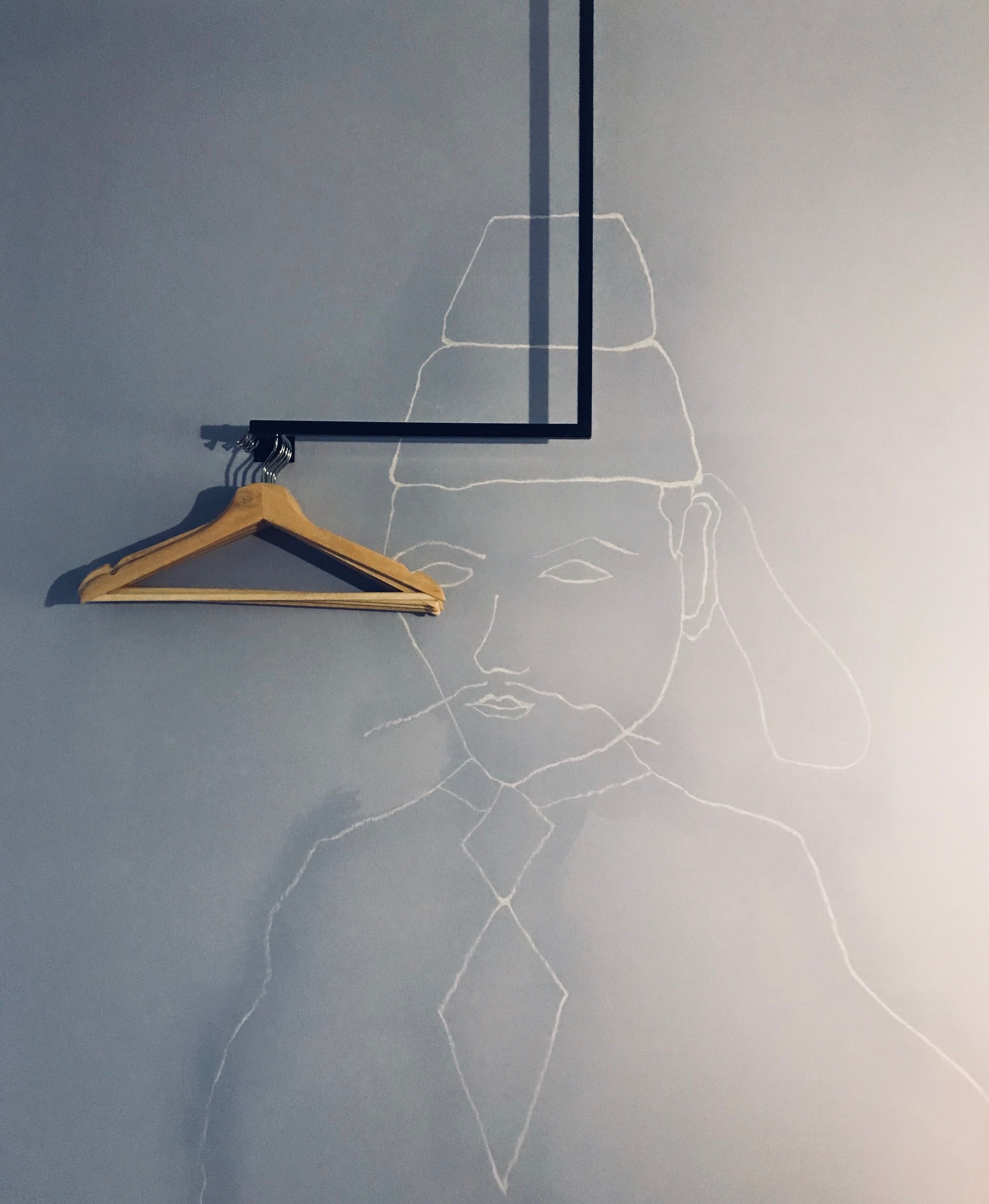A wall with a chalk outline of a person wearing a hat and a tie, a wooden hanger, and a black frame.