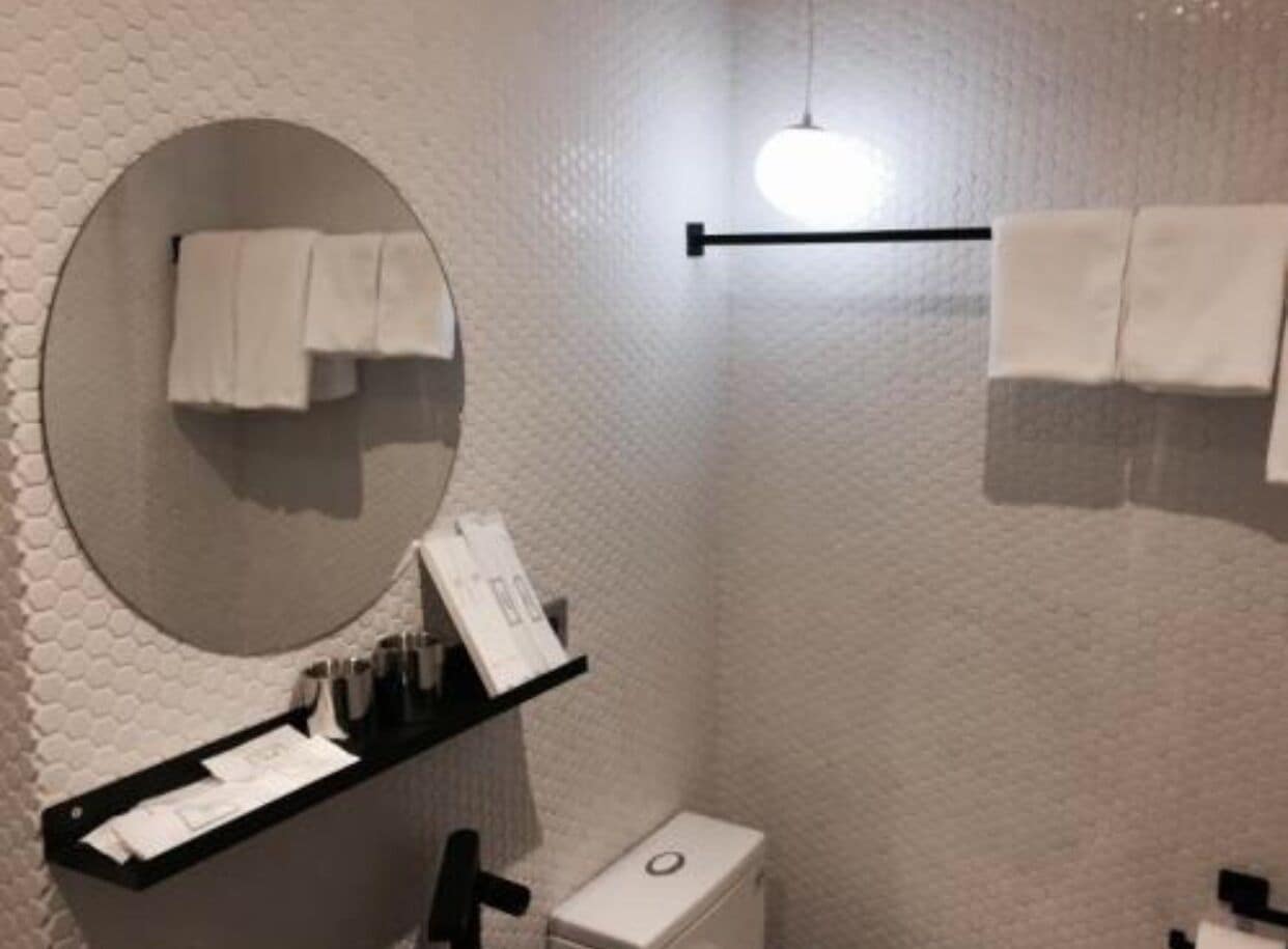 A bathroom with a round mirror, a towel rack, and a shelf with toiletries.
