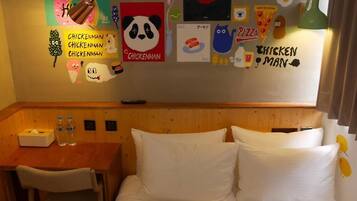 A hotel room with a wooden headboard, a small table with two bottles of water, a tissue box, and a wall decorated with various cartoon characters and words like "CHICKENMAN" and "PIZZA".