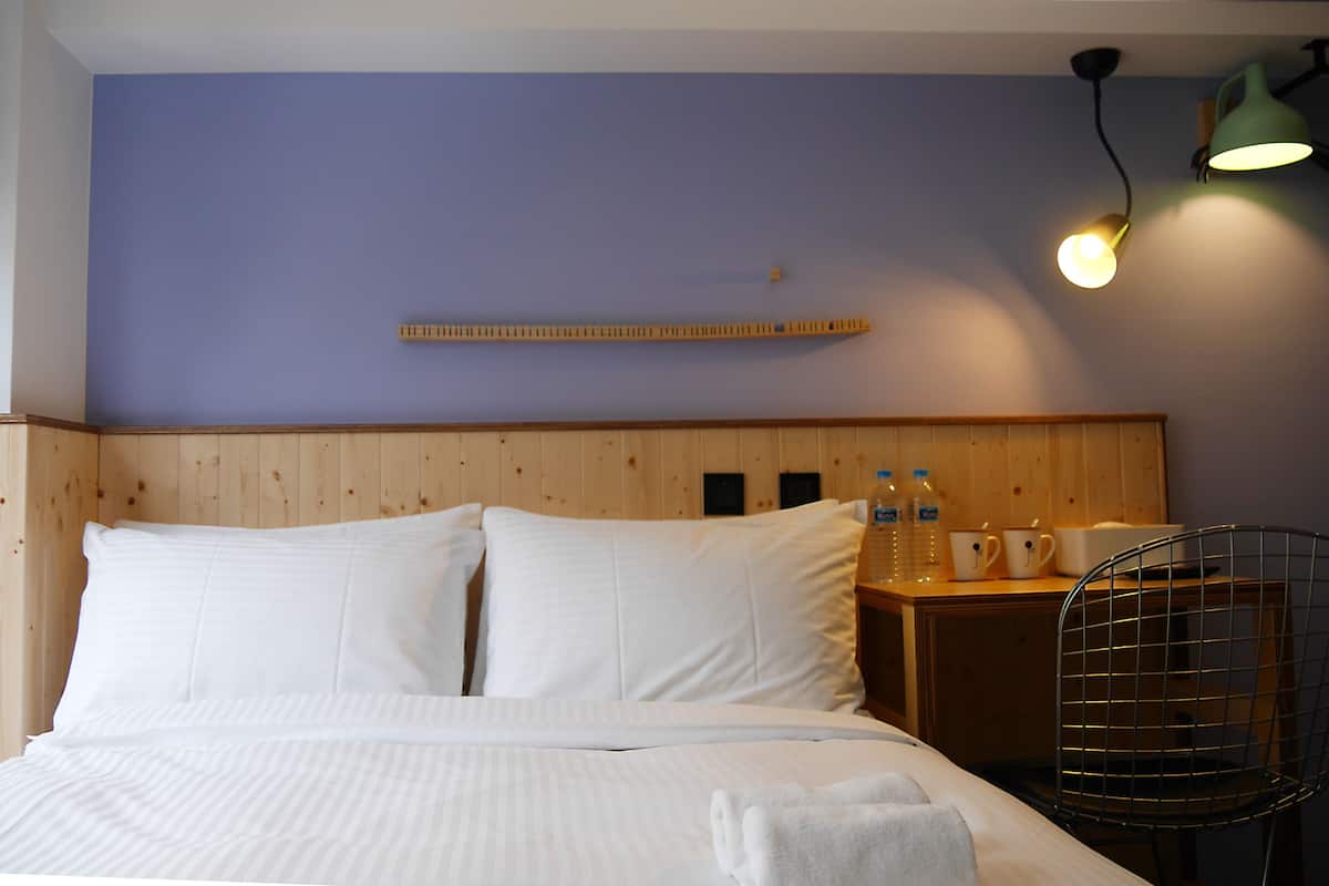 A neatly made bed with white linens, a wooden headboard, a bedside table with a lamp, and a chair.