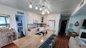 Una cocina con armarios blancos, encimera de granito y una isla central con taburetes de bar. Incluye un microondas, horno y refrigerador.