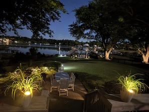 A nighttime outdoor seating area with a view of a lake, a dock, and a distant building.
