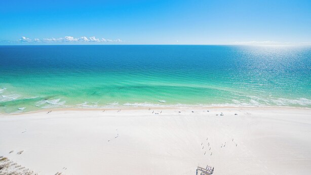 A beach with clear turquoise water and a wide sandy shore. - The Oasis at Orange Beach, formerly known as Phoenix West II, Unit 2310 (Orange Beach)