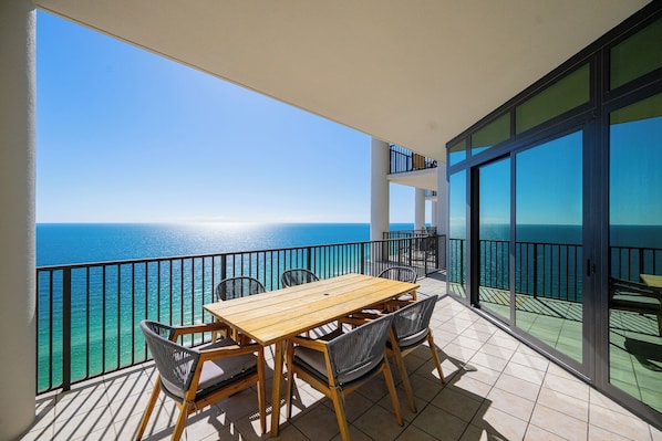 A balcony with a wooden table and chairs, overlooking a clear blue sea.