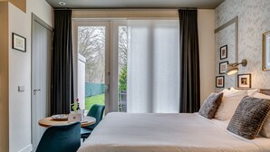 Une chambre à coucher avec un lit, un bureau et une chaise. Il y a une fenêtre avec des rideaux, une porte et un mur orné de tableaux.