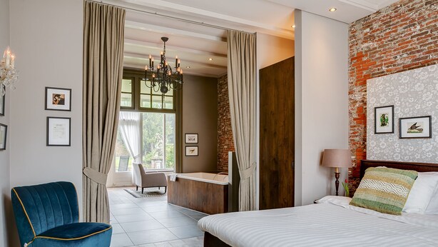 Une chambre moderne avec un grand lit, une chaise bleue, un bureau en bois et une vue sur un balcon.
