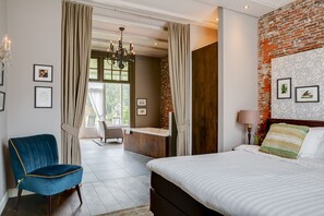 A modern bedroom with a large bed, a blue chair, a wooden desk, and a view of a balcony. - Boutique Hotel 't Vosje (Business & Leisure) (Haarlem)
