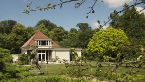 Une maison avec un toit rouge, entourée d’une végétation luxuriante et d’arbres.