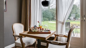 Une table de petit-déjeuner avec un plateau de nourriture, deux chaises et une vue sur un jardin par la fenêtre.