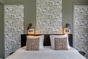 A neatly made bed with two patterned pillows, a dark headboard, and a wall decorated with framed certificates. - Boutique Hotel 't Vosje (Business & Leisure) (Haarlem)