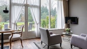 Un salon moderne doté d’une grande fenêtre, d’un téléviseur à écran plat et d’un coin repas avec une table et des chaises.