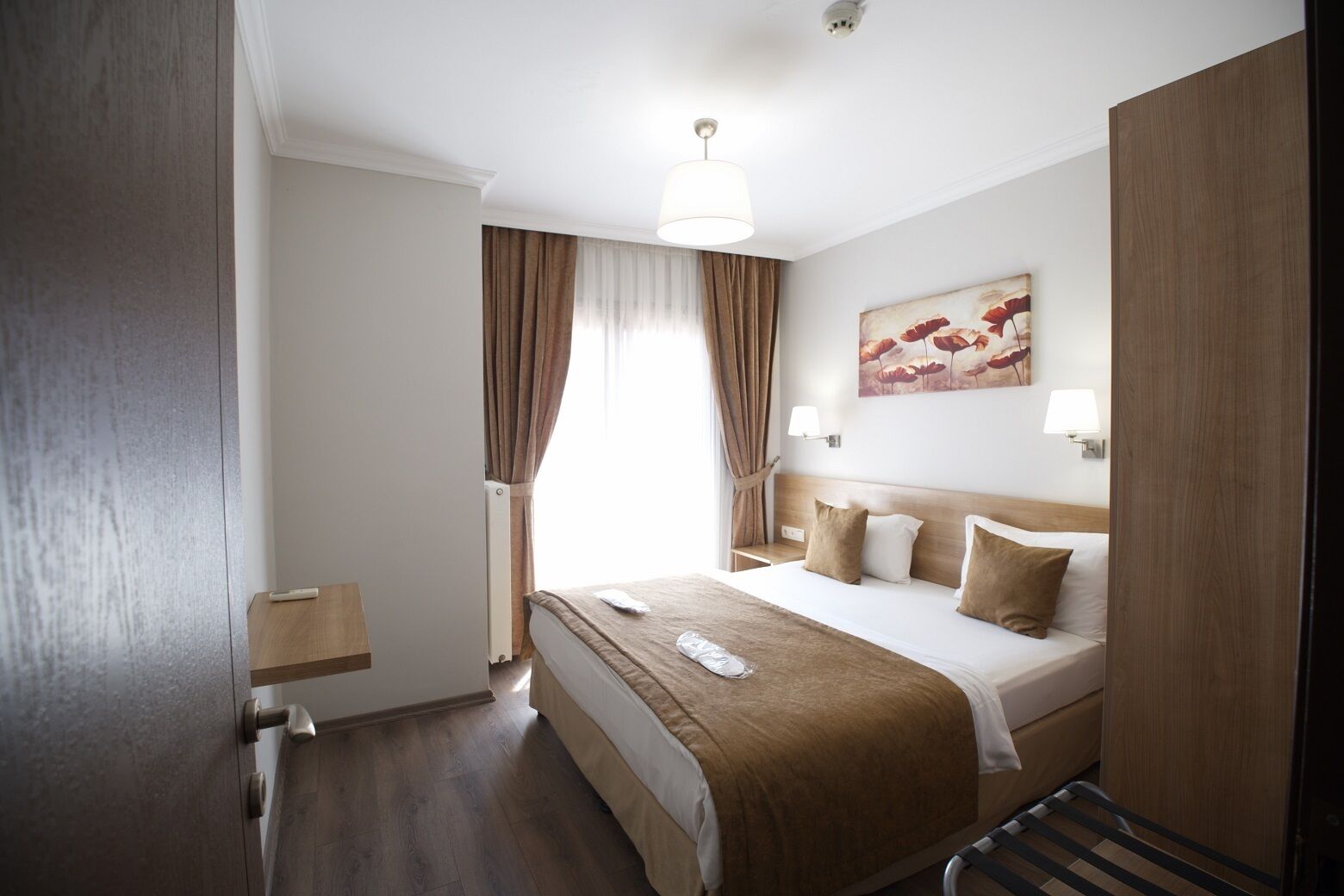 A hotel room with a bed, bedside lamps, a painting, and a window with curtains.