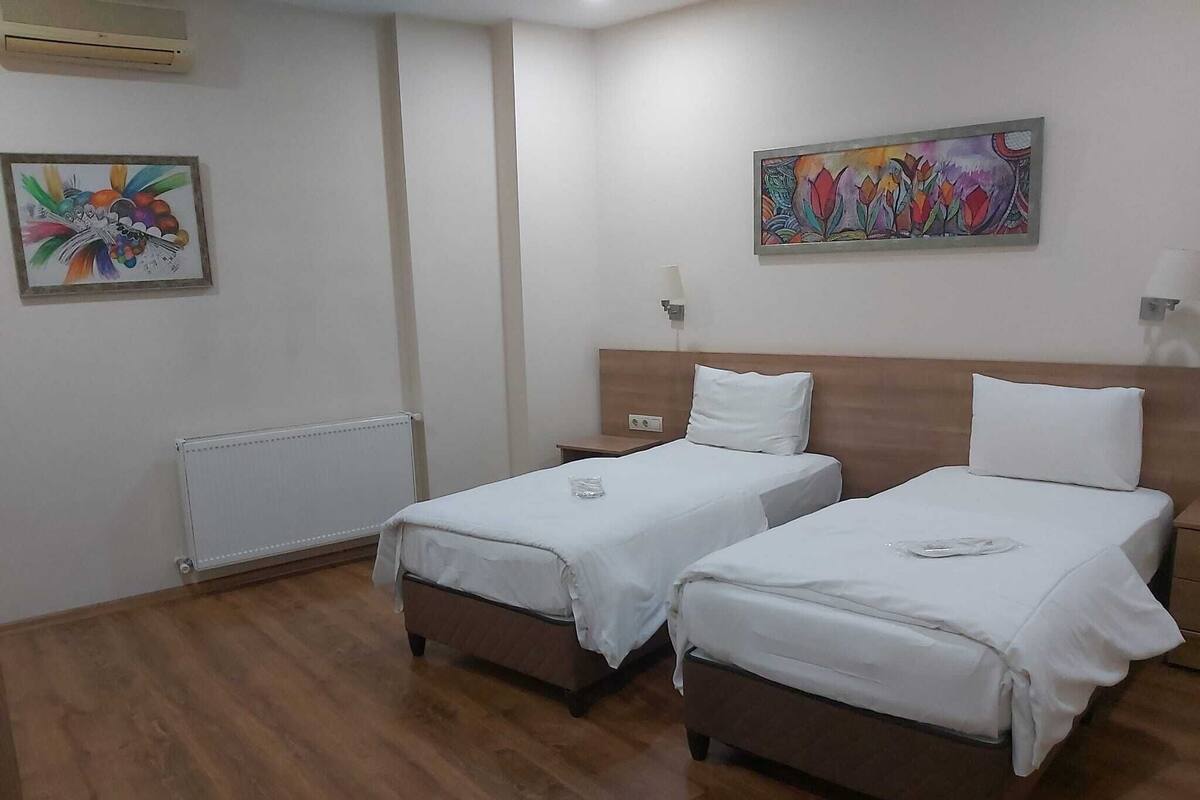 A hotel room with two beds, a radiator, a painting, and a nightstand.