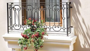A balcony with a wrought iron railing, a window with a curtain, and a hanging flower basket.