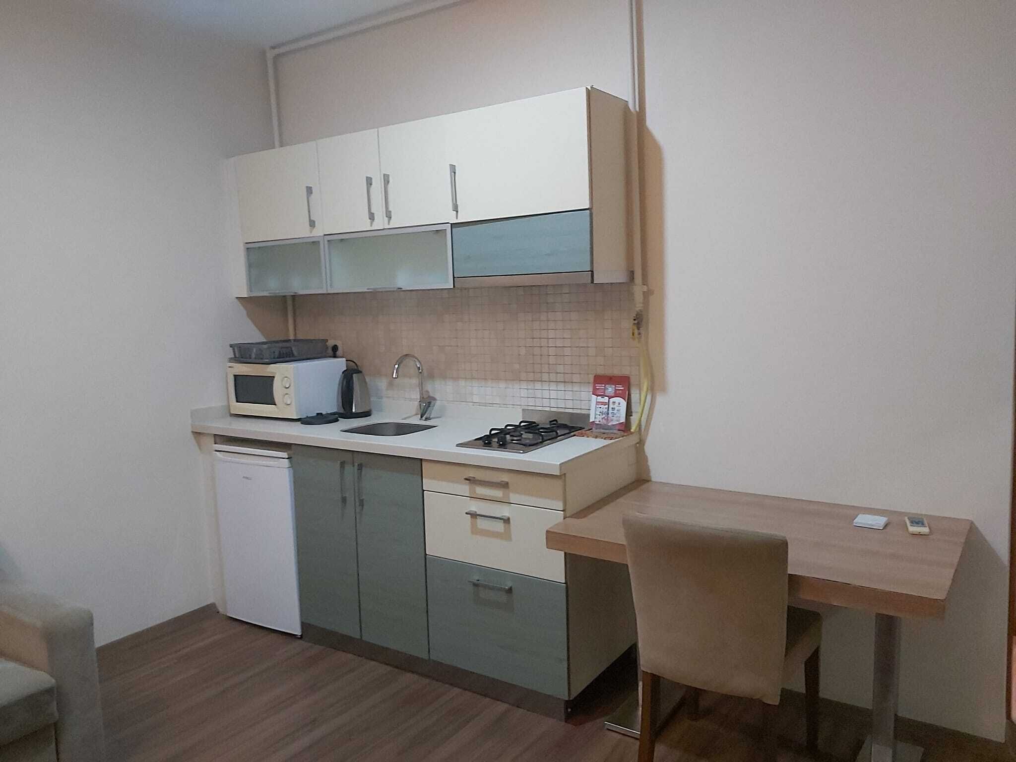 A compact kitchen with a microwave, toaster, sink, and a small dining table with a chair.