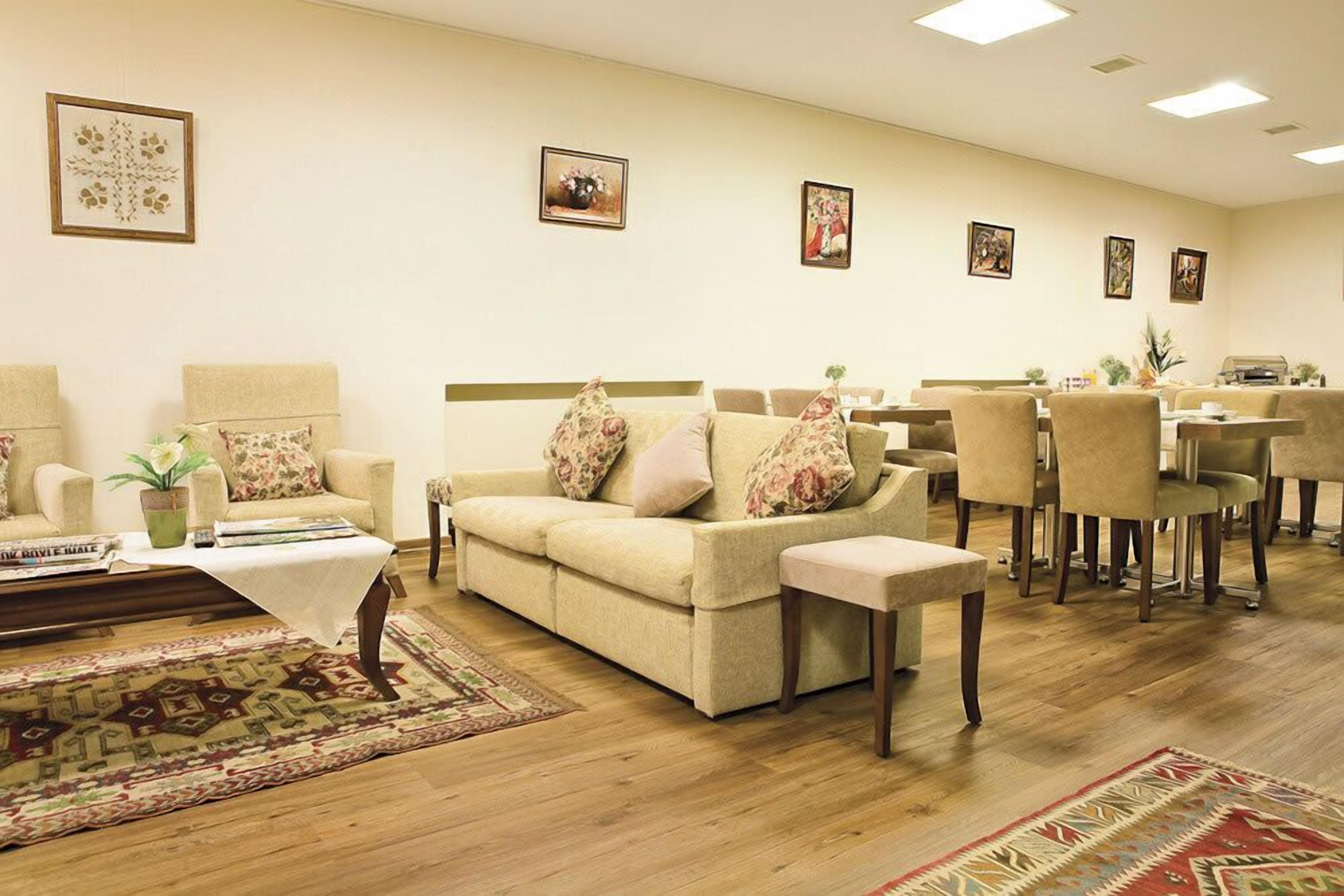 A hotel room with a sofa set, a dining table with chairs, a small table with a plant, and a patterned rug.